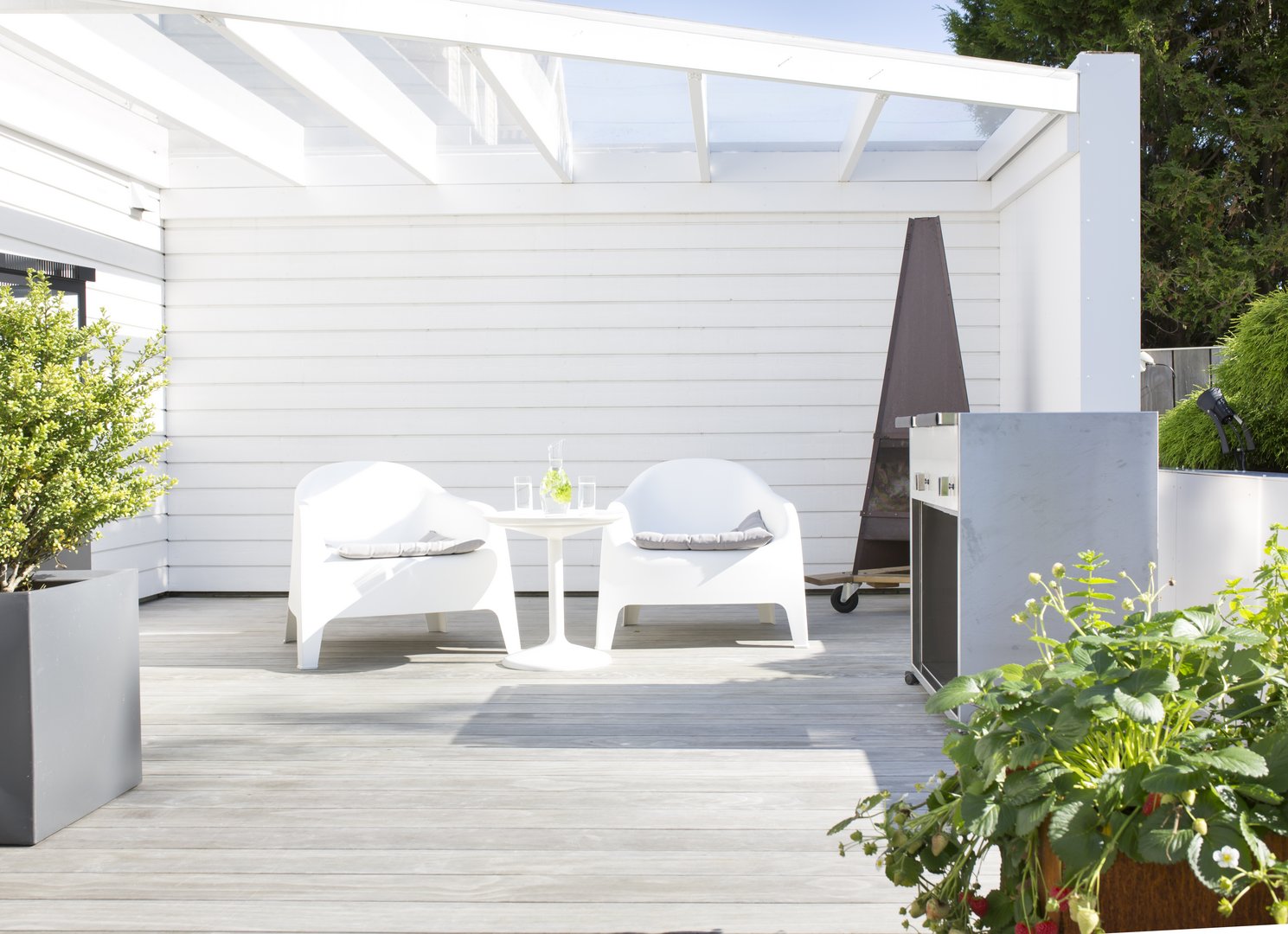 Kebony Clear Terrassendielen - extrem pflegeleichte Terrassen Bild einer hellen Ecke am Haus mit einer hellen Holzterrasse und 2 weißen Stühlen - überdacht