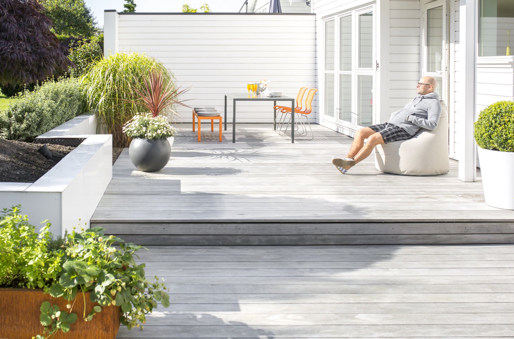 Kebony Clear Terrassendielen - nachhaltige und langlebige Qualitätst-Terrassen Ein Mann genießt die Sonne auf seiner hellen Holzterrasse sitzend